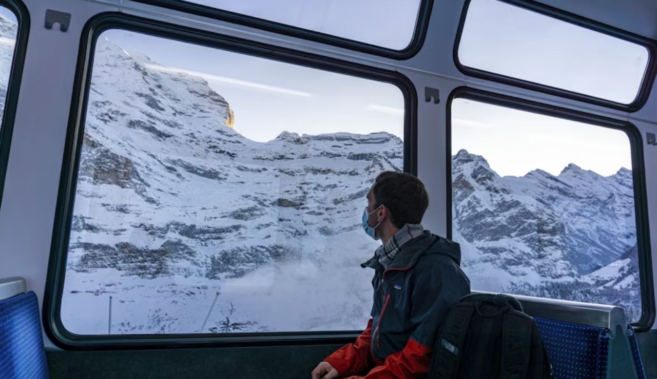 A person sitting in a train cabin, gazing at snow-covered mountains through the window.