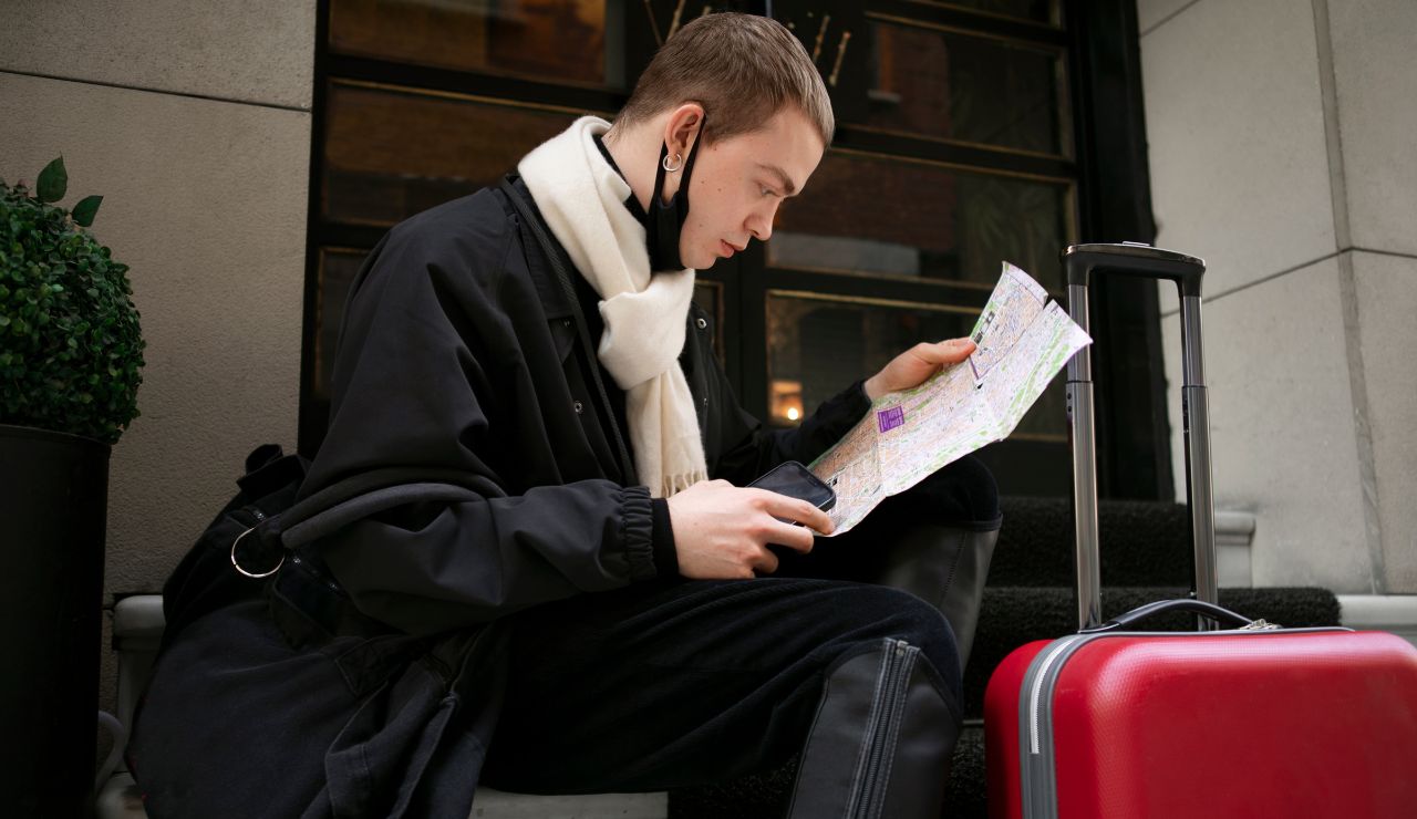 A traveler holding a printed hotel confirmation and shrugging with luggage nearby.