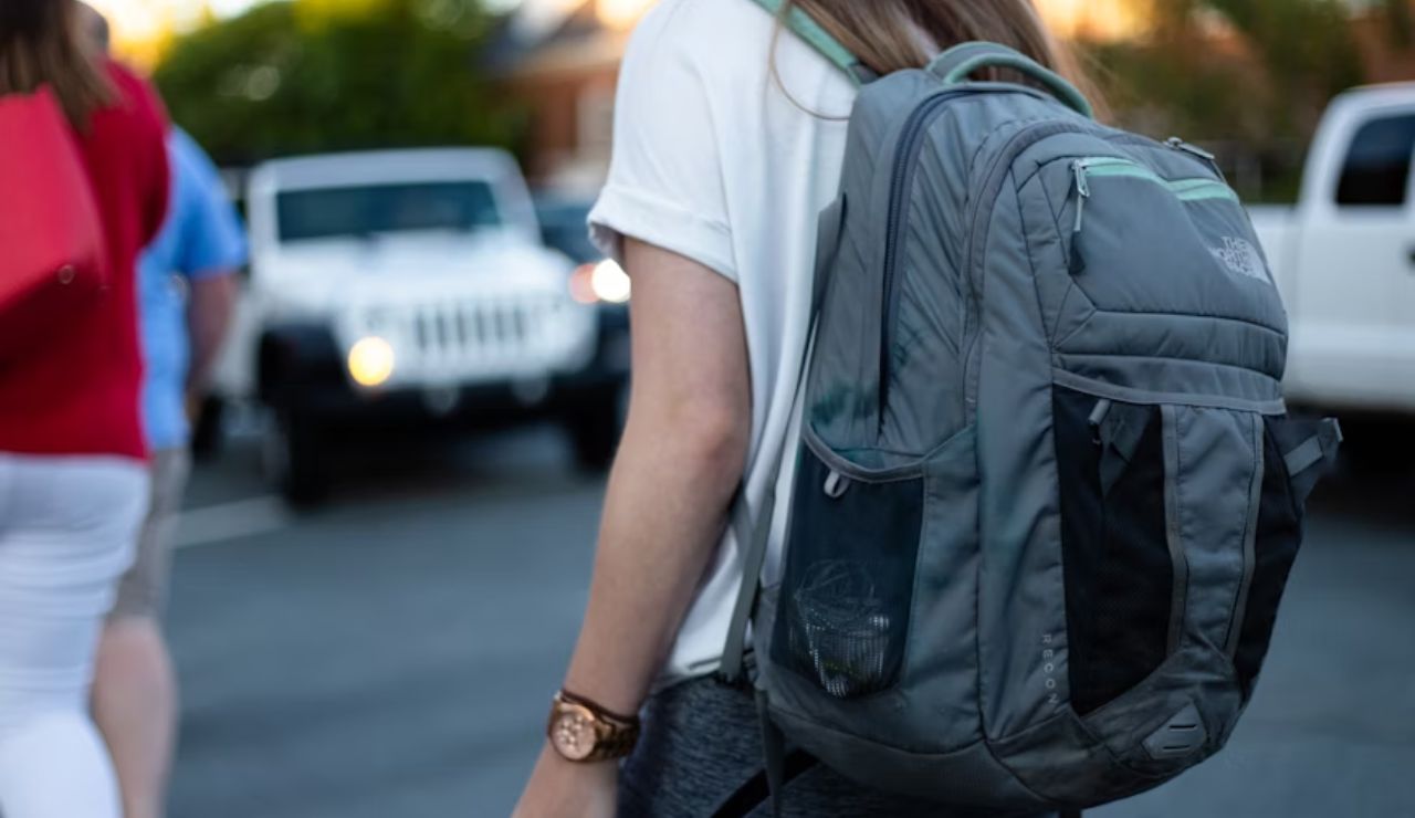 Close-up of a person wearing a large gray backpack while walking in a parking lot.