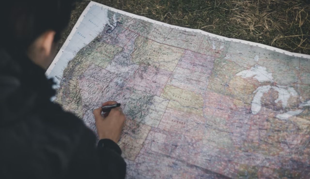 Person marking a large map of the United States with a pen while outdoors on the grass.