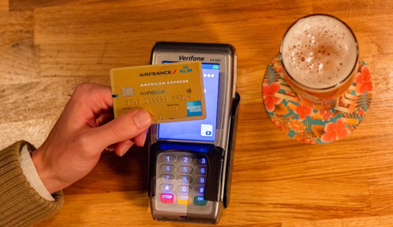 Person holding a credit card over a payment terminal next to a glass of beer.