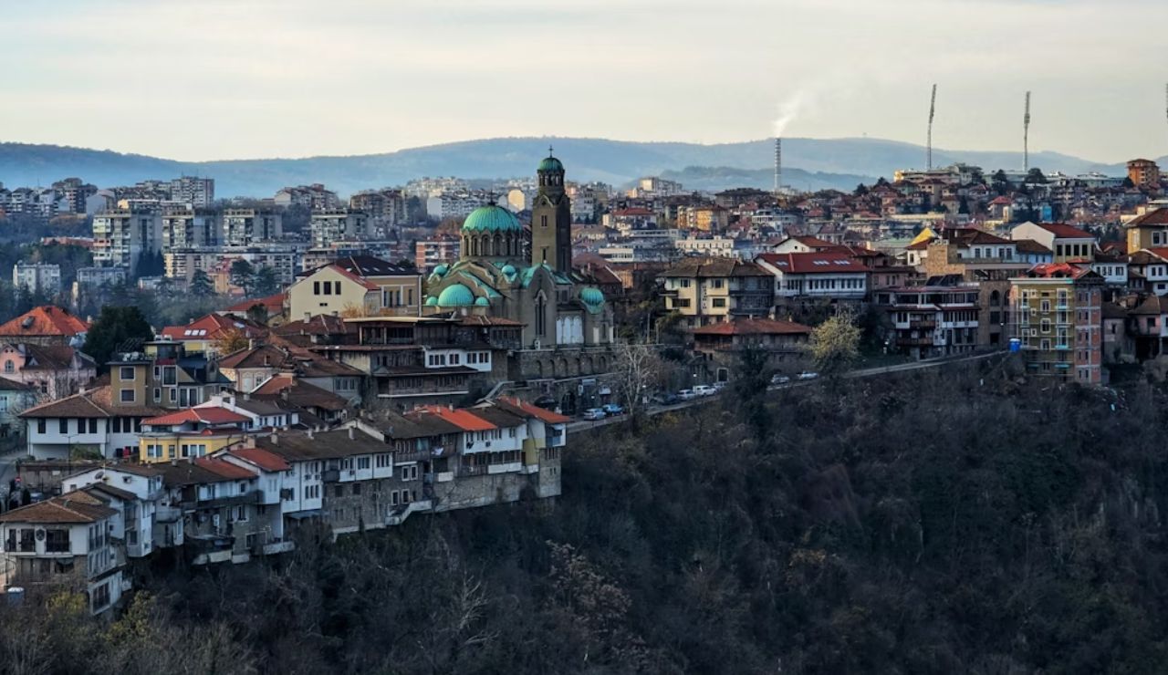 Panoramic view of Veliko Tarnovo, Bulgaria, featuring cliff-side houses and a domed Orthodox cathedral rising above the town.