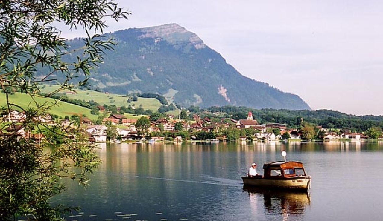 Small boat on Lake Sarnen with a village and mountain backdrop in Switzerland.