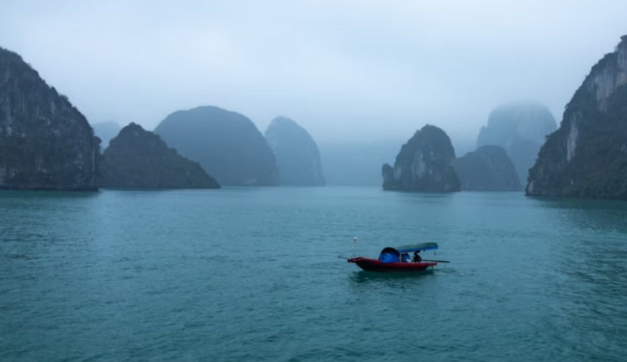 Small boat floating in Ha Long Bay surrounded by misty limestone islands.
