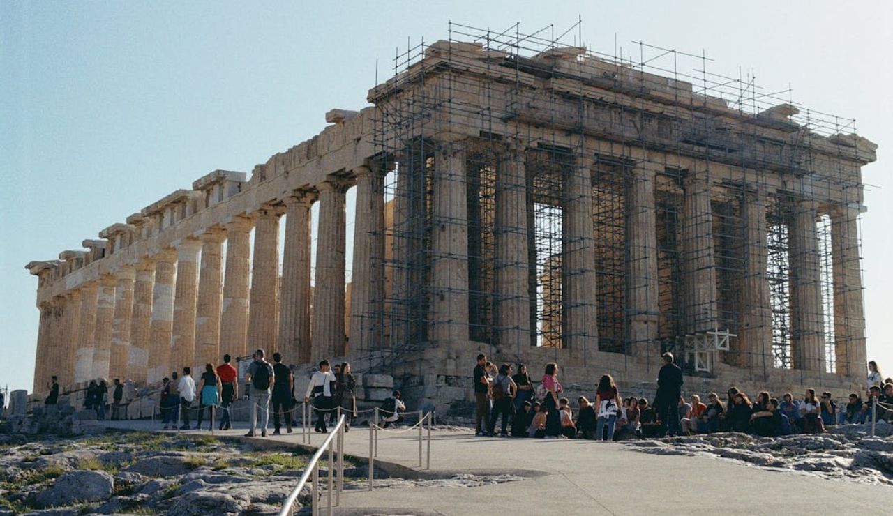 Parthenon temple in Athens under restoration with scaffolding, surrounded by tourists on a sunny day.