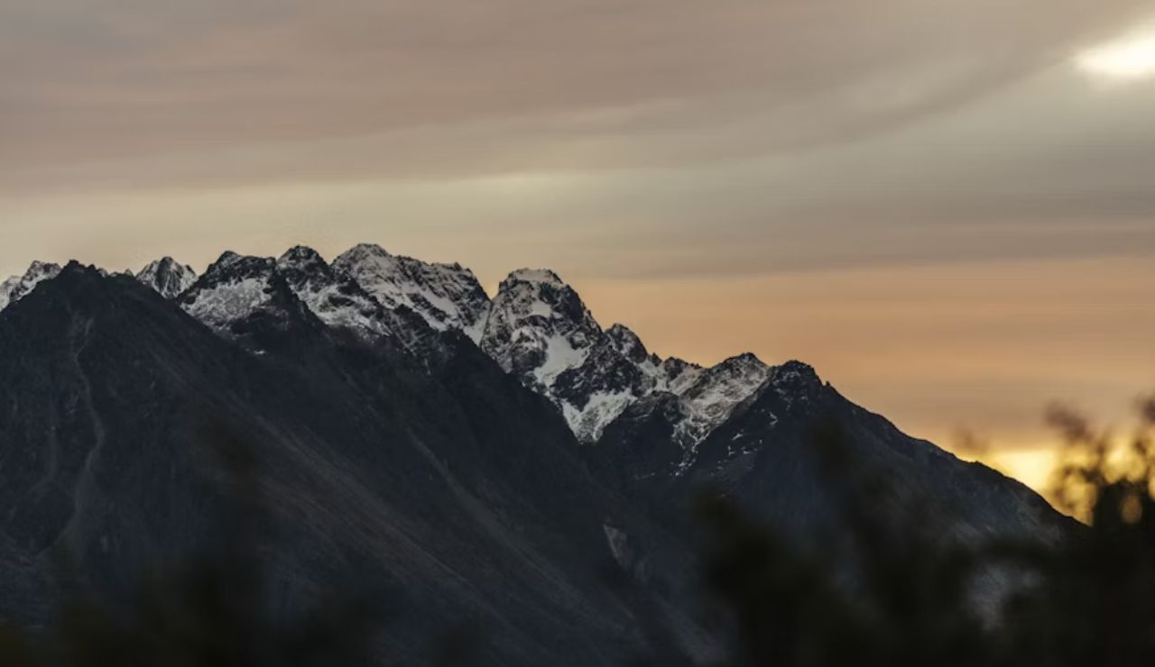 Snow-capped mountain peaks under a dramatic sky during sunset or sunrise.
