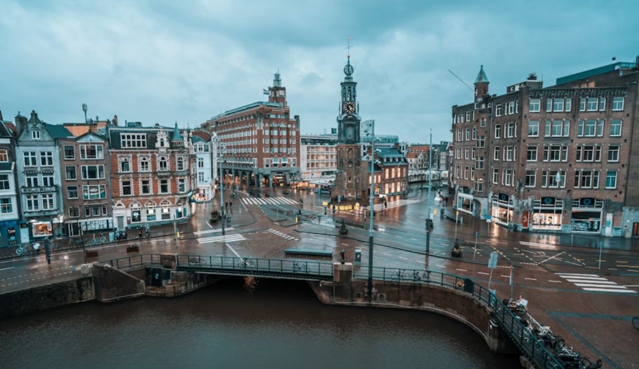 A quiet, rainy morning in Amsterdam featuring historic buildings, a canal, and the Munttoren clock tower.