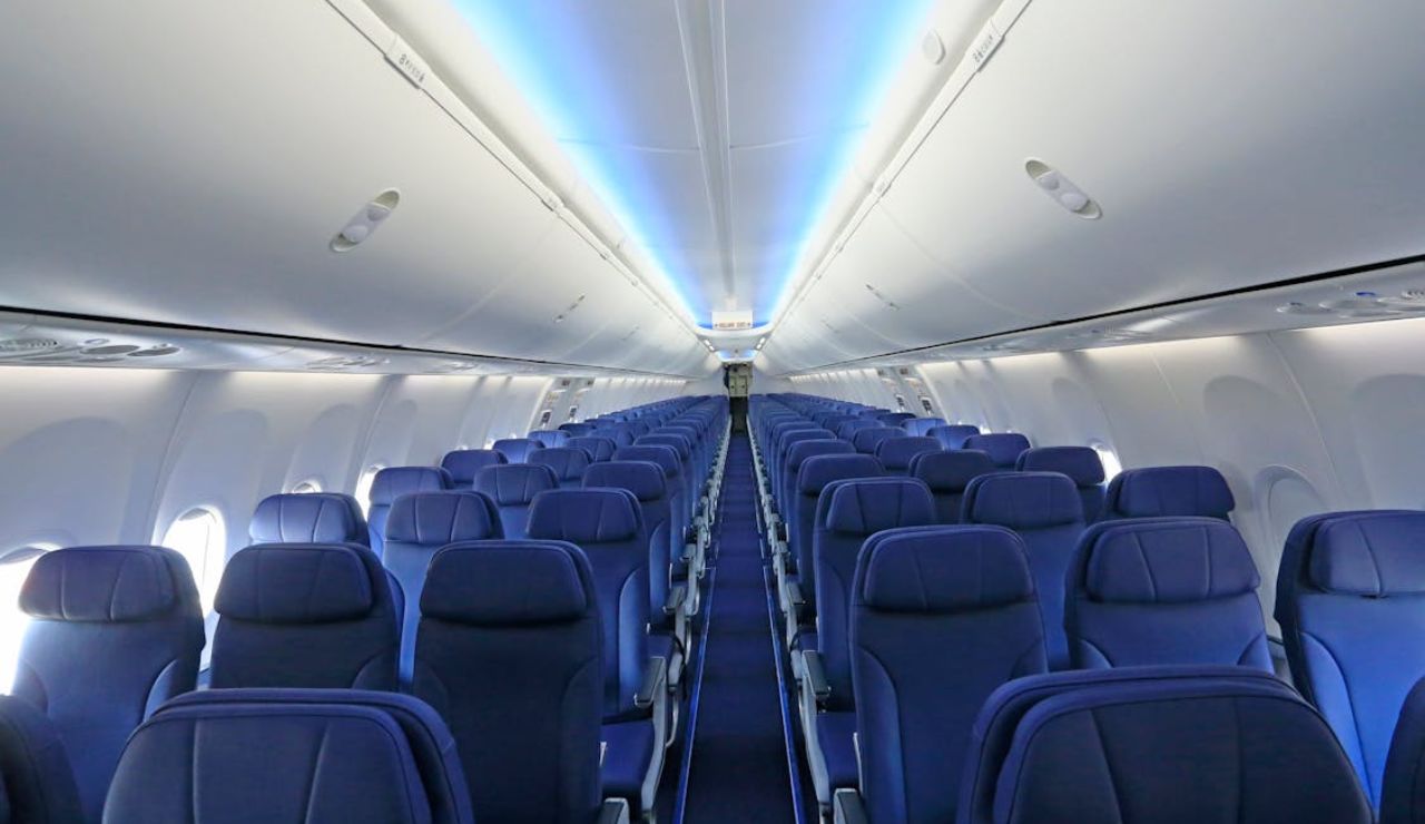 mpty airplane cabin with rows of blue seats and overhead storage, viewed from the back looking toward the front.