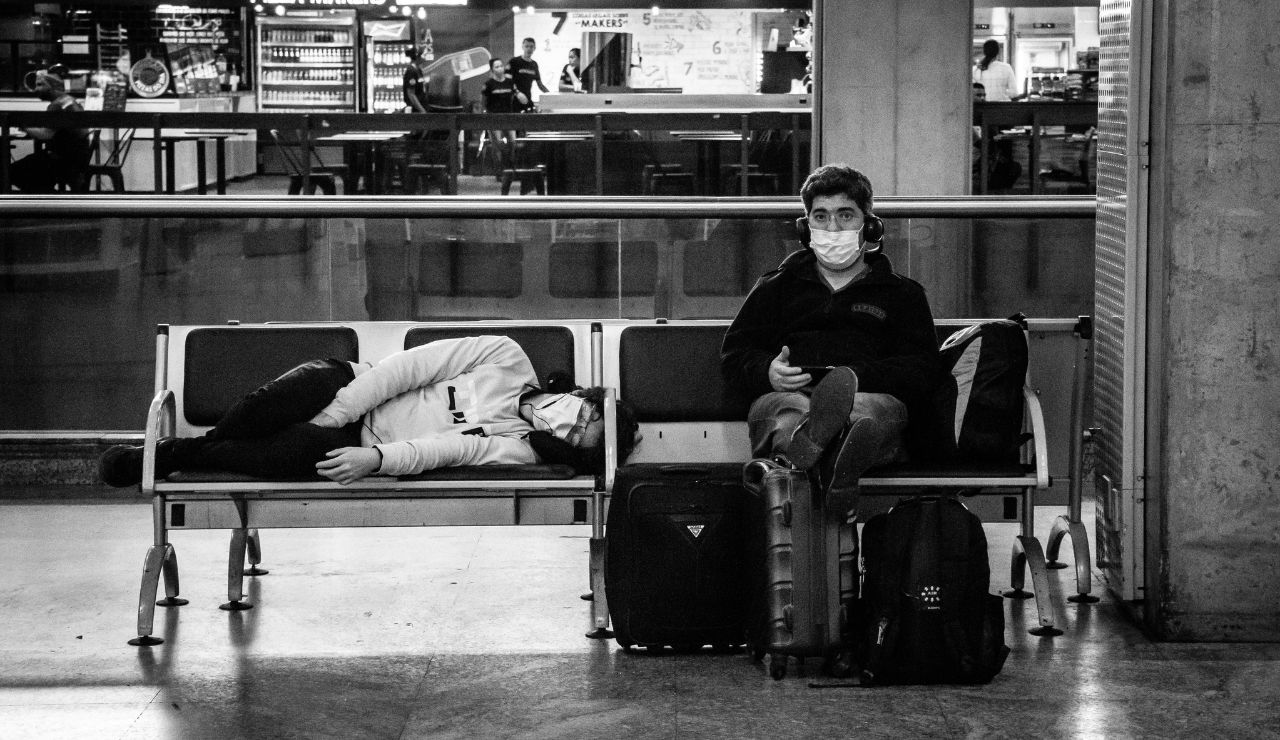 Traveler sleeping on an airport bench with eye mask and neck pillow