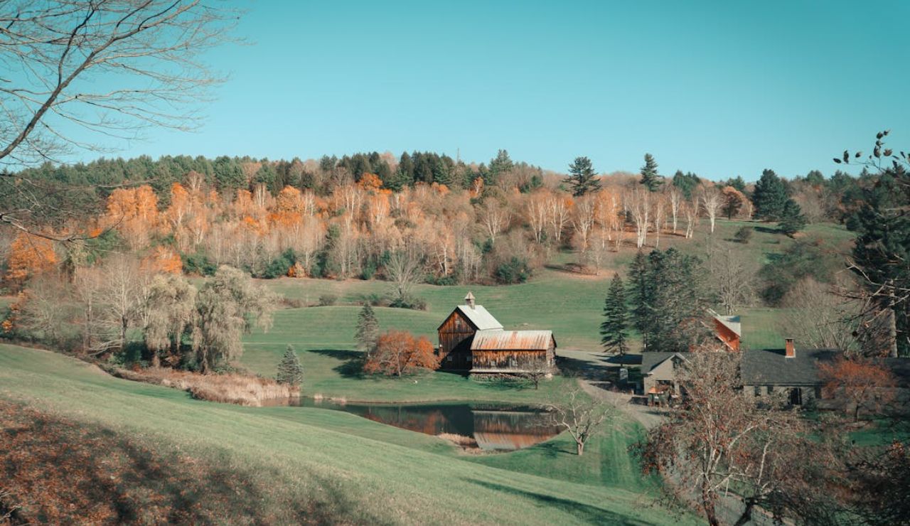 Scenic countryside landscape with rustic barns, a pond, and colorful autumn trees.