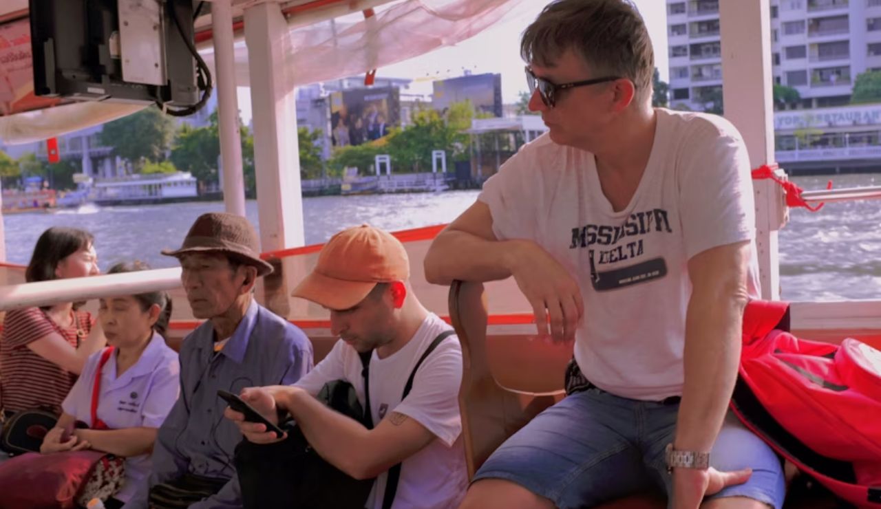  Passengers sit on a river cruise boat, with one man using a mobile phone while others relax and enjoy the view.