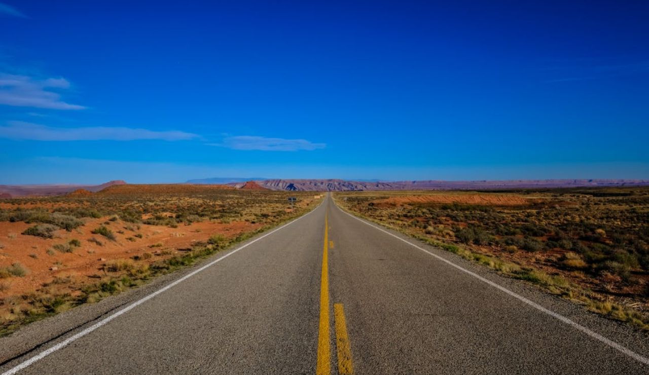 Open desert highway stretching between Zion and Bryce Canyon in Utah under a clear blue sky.