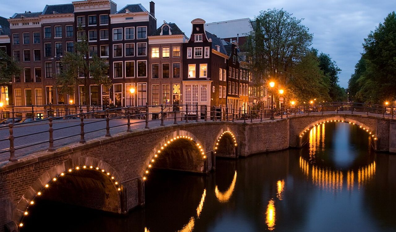 Night-lit canal bridge reflecting under gabled houses in Amsterdam