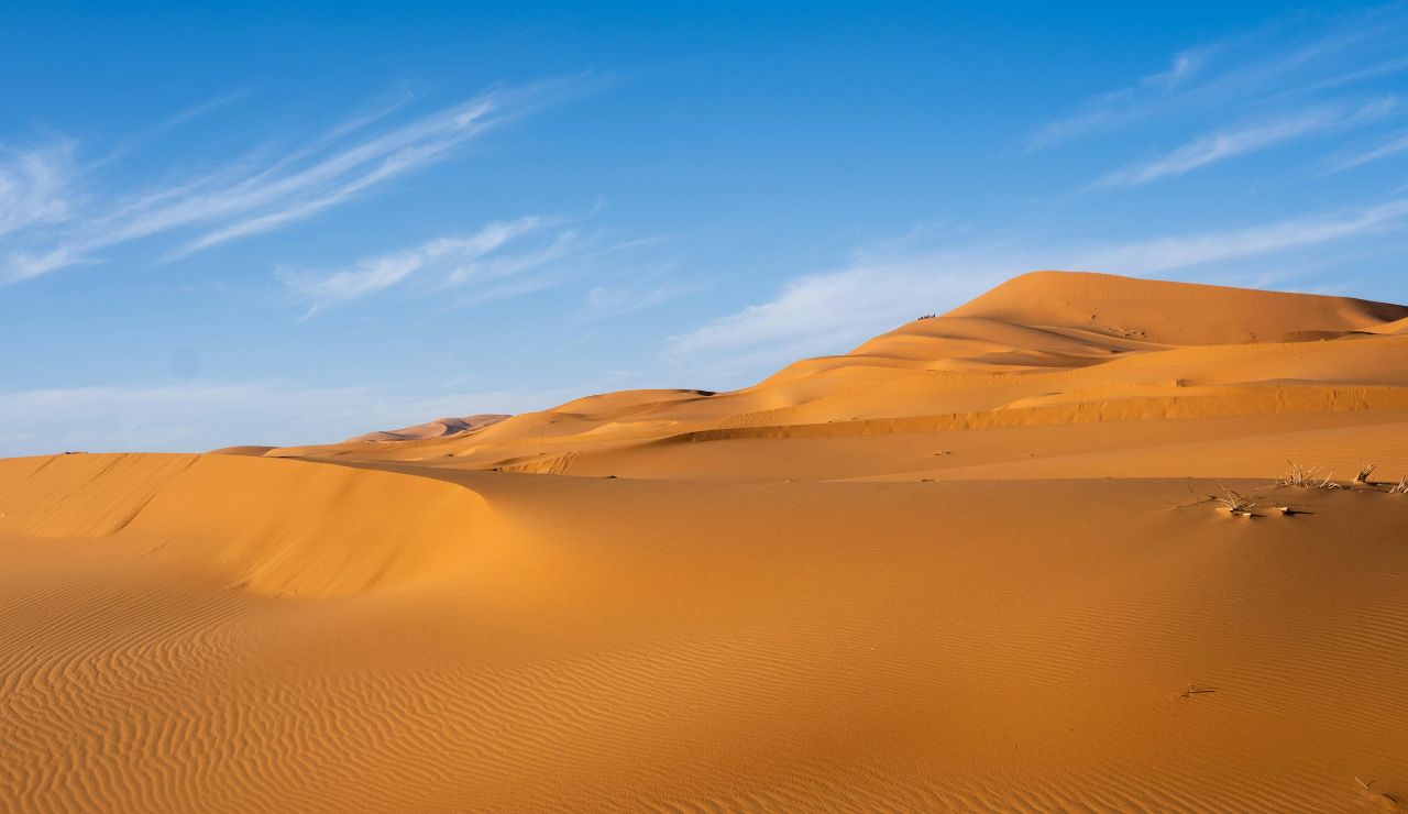 Replica steam engine on desert track under a bright blue sky or wide open plain with railroad running into horizon.