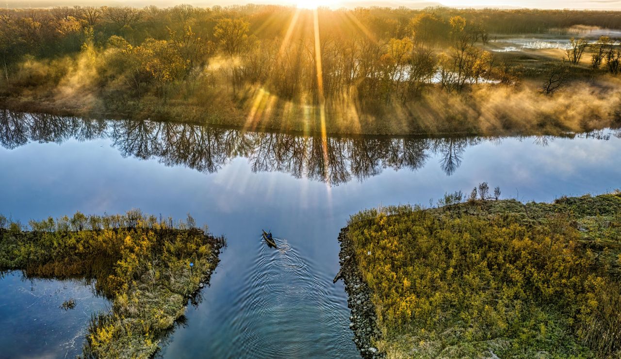 Calm lake at sunrise or sunset with mist or light reflecting on the water; possibly a kayak in the distance.