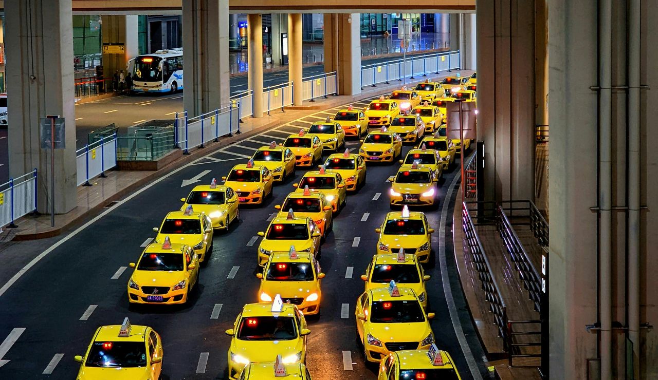 Row of yellow taxis waiting outside a busy airport terminal