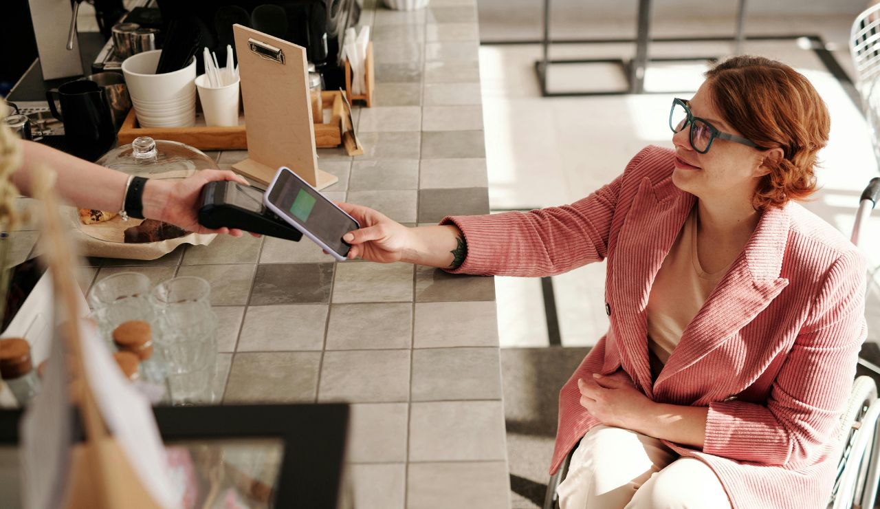 Close-up of a person paying with a mobile phone at a Nordic café counter, showing contactless payment in action