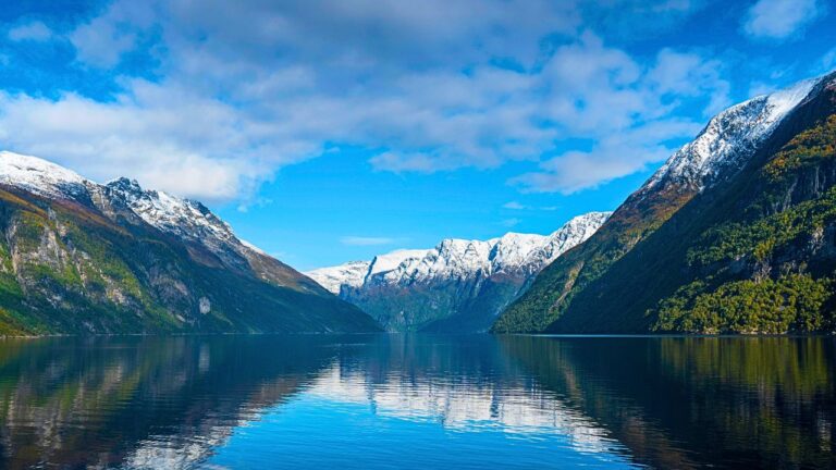 Sweeping panoramic view of Nordic fjords with mountains, forests, and a calm waterway under a cloudy sky