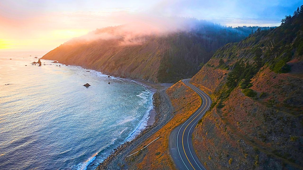 A sweeping aerial view of Ortega Highway snaking through the Santa Ana Mountains at golden hour, showing the blend of beauty and elevation changes.