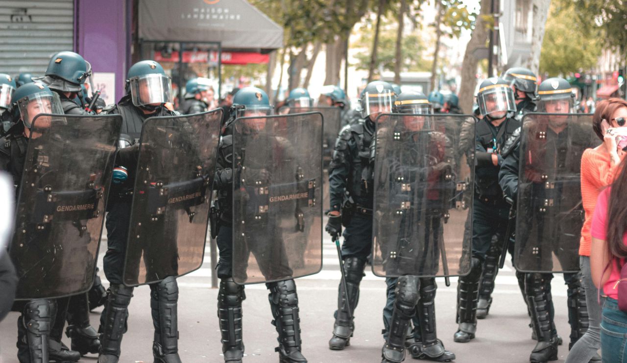 A protest scene with police and signs near a landmark, viewed from a tourist's perspective.