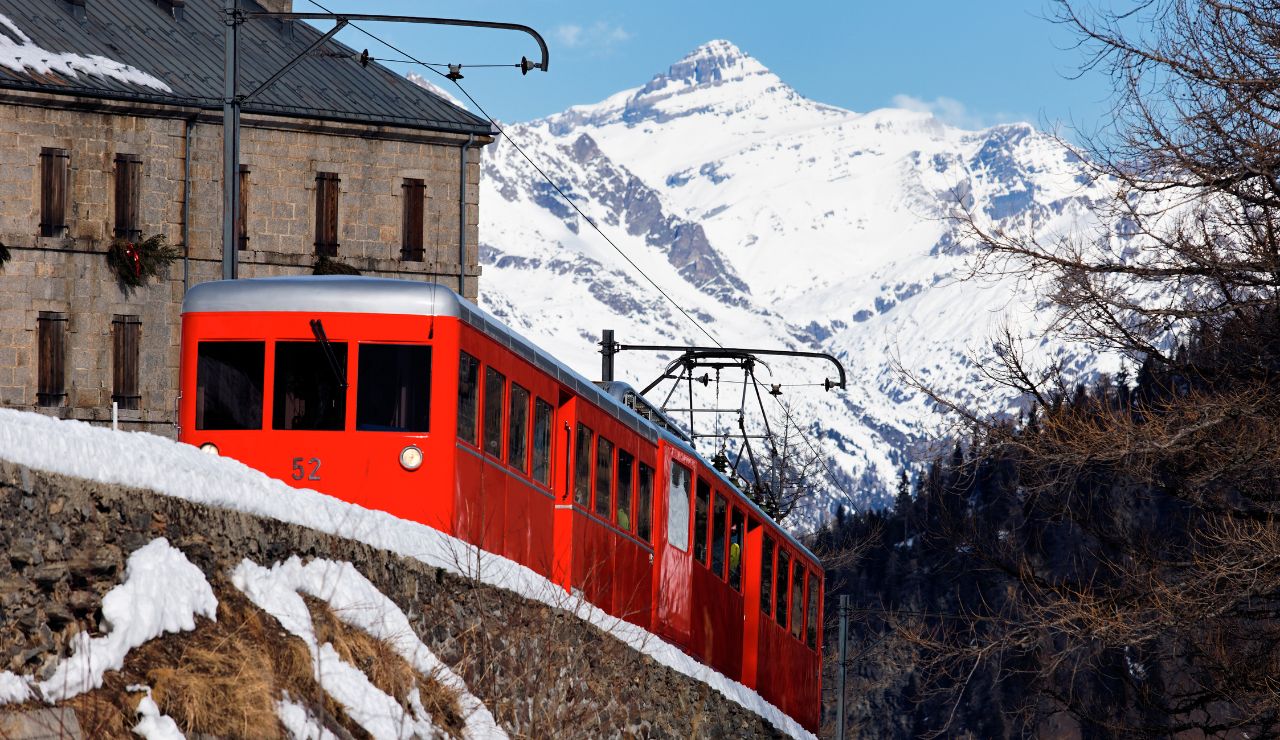 Historic narrow-gauge train crossing a wooden trestle with glaciers and steep mountains in the background.