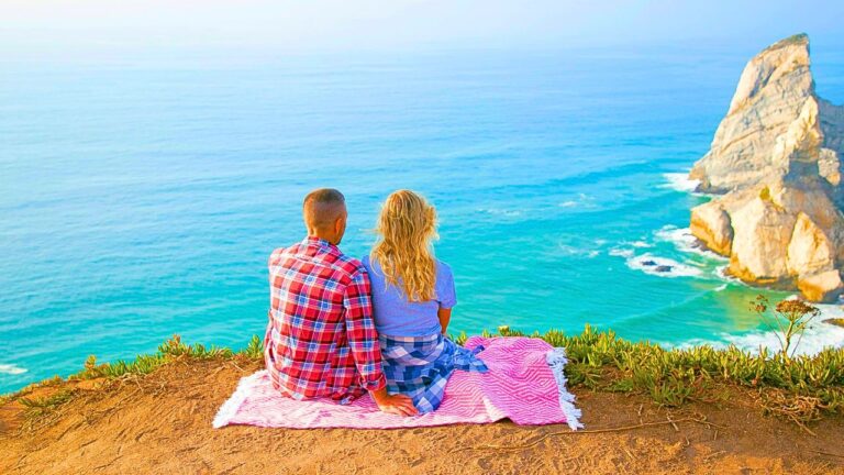 Couple hiking along a scenic coastal trail in New Zealand with ocean cliffs and blue skies.