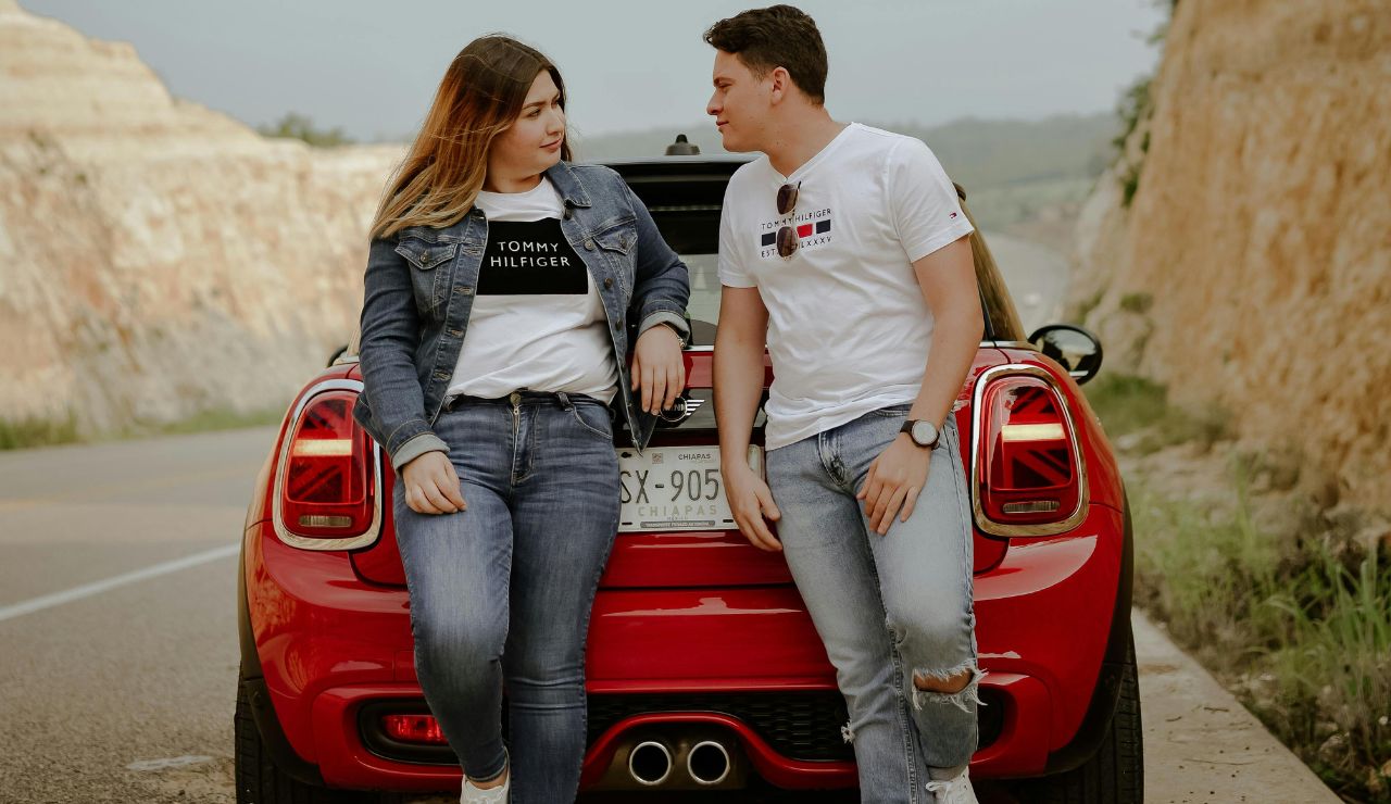 A couple at a roadside stop switching drivers beside a rental car during a summer road trip.