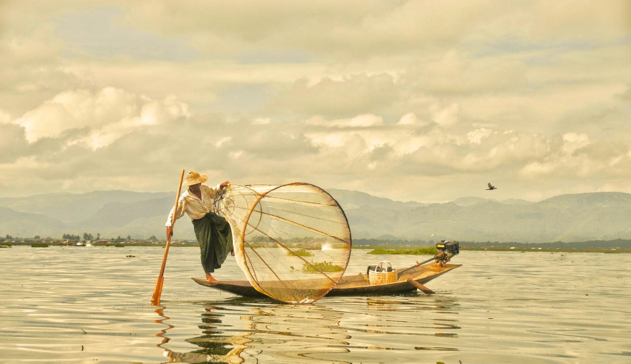Intha fisherman rowing on Inle Lake with floating homes in the background