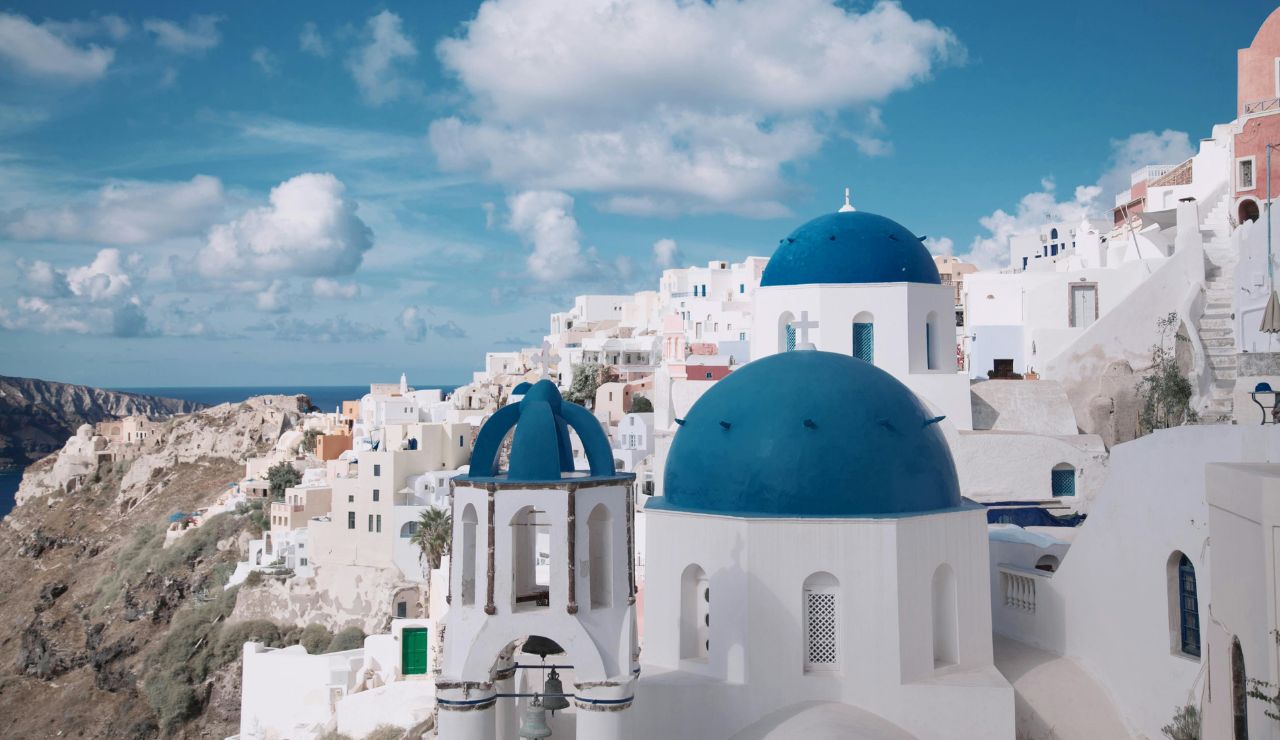 Blue-domed church in Santorini overlooking the Aegean Sea at sunset.