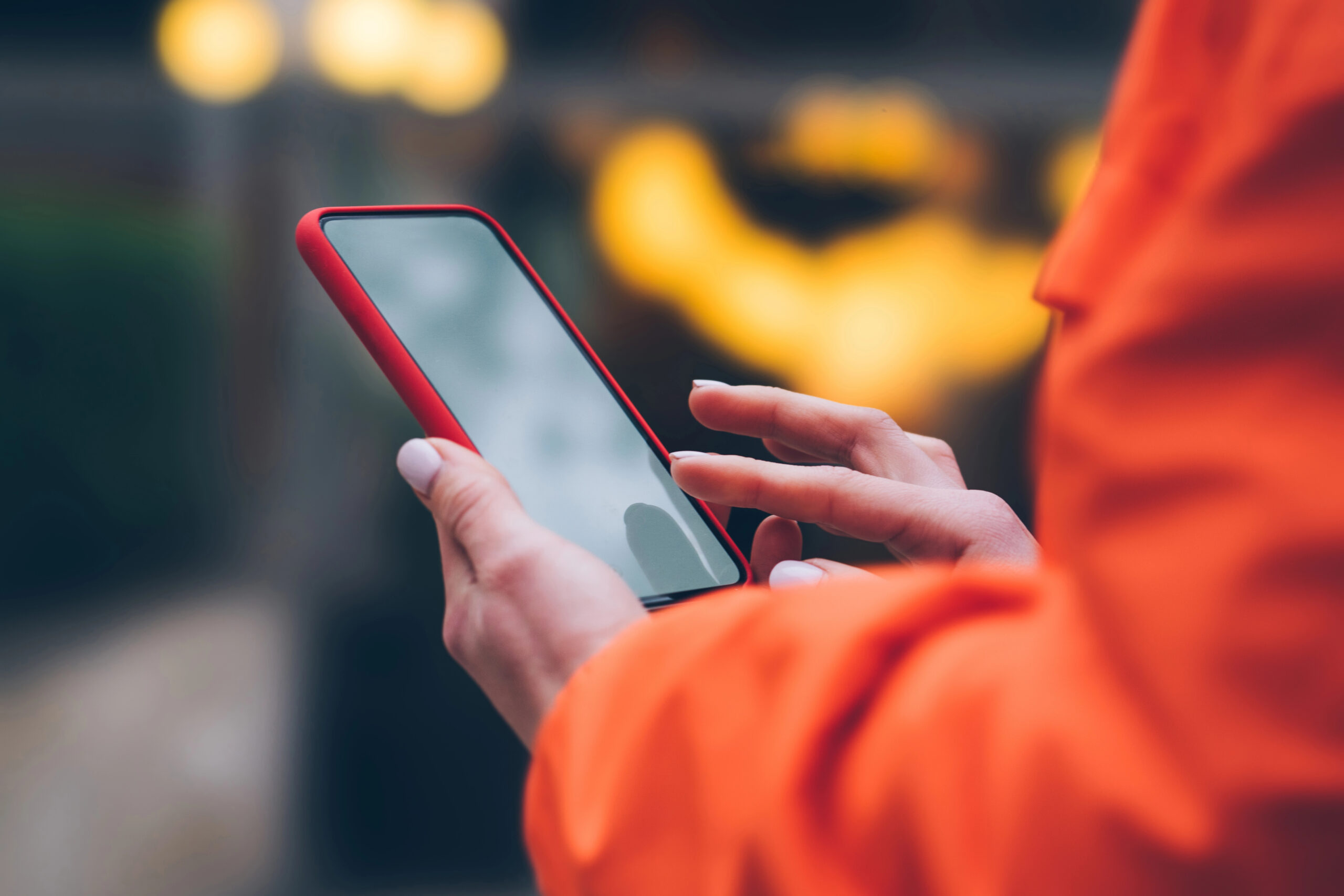 A woman on her iPhone with an orange coat.