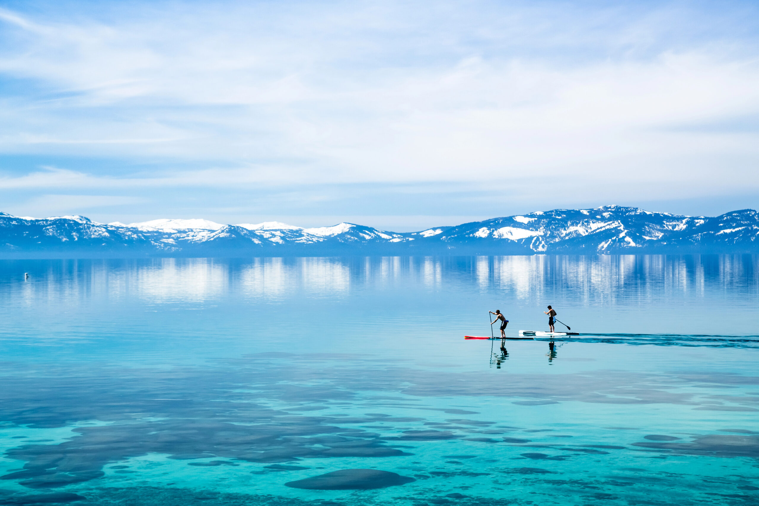 A couple paddle boarding on the lake in the winter in Lake Tahoe.