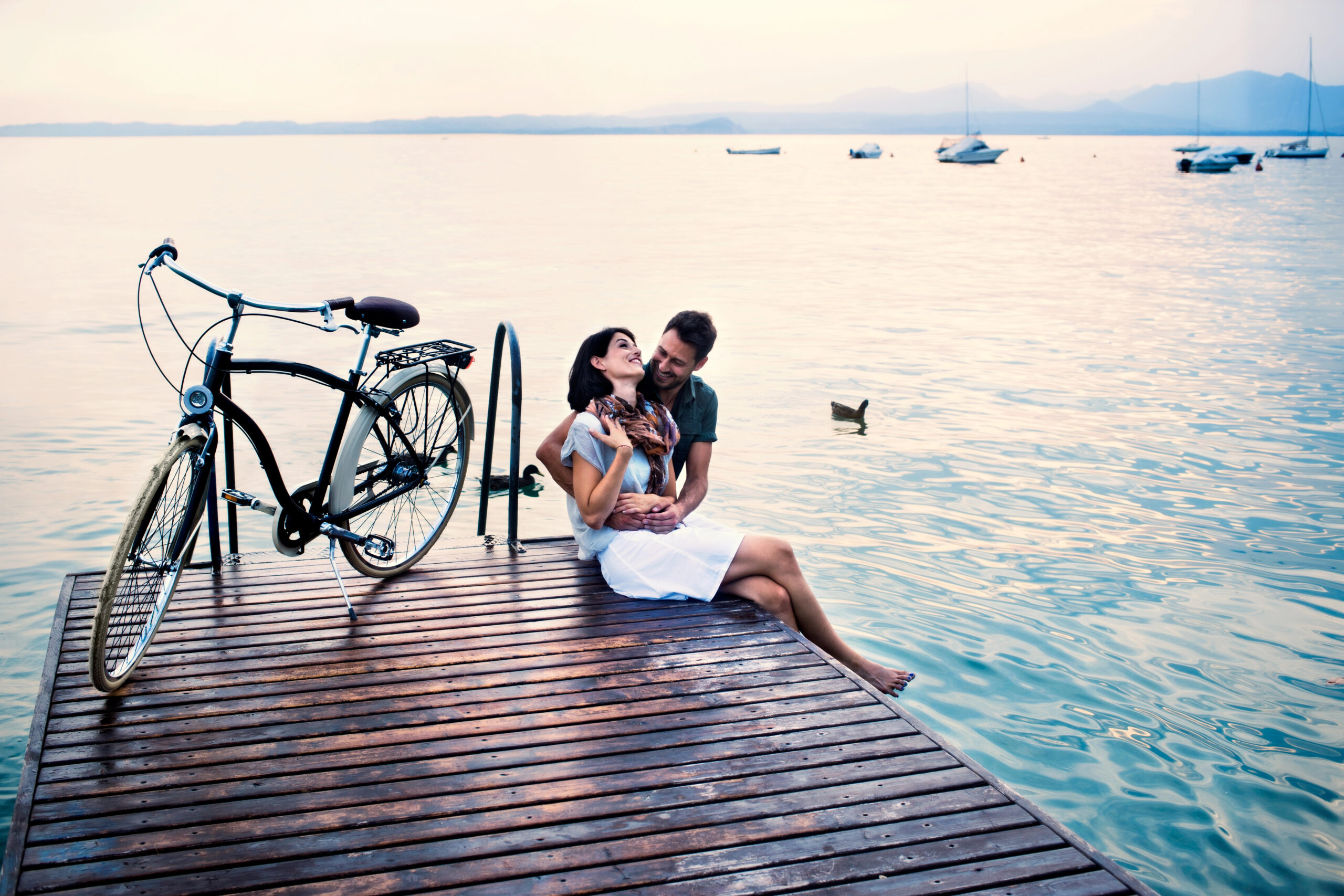 A couple embracing on a dock with a bicycle.