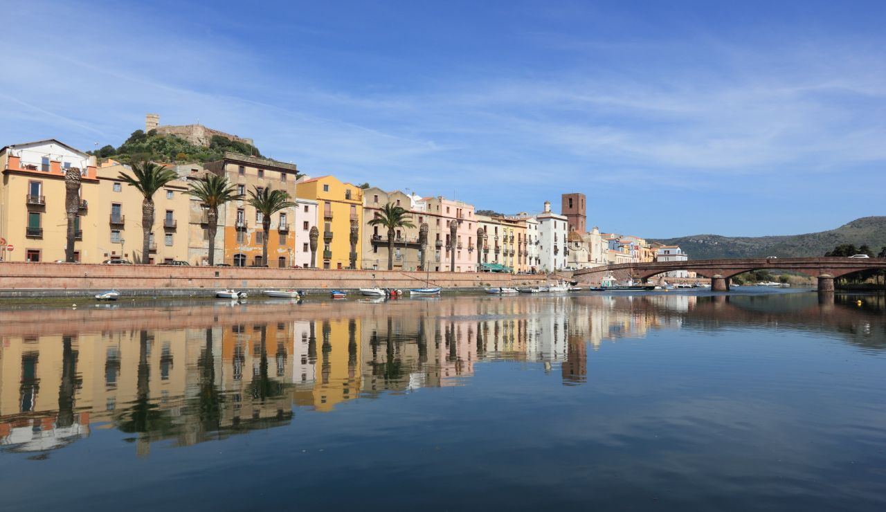Colorful riverside buildings in Bosa, Sardinia, reflected in calm water.