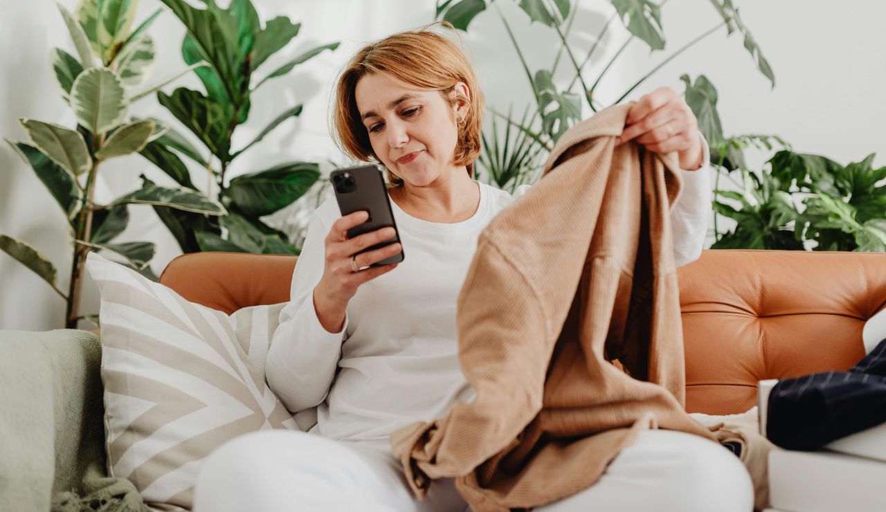 Person packing suitcase while checking weather forecast and dress code on phone.