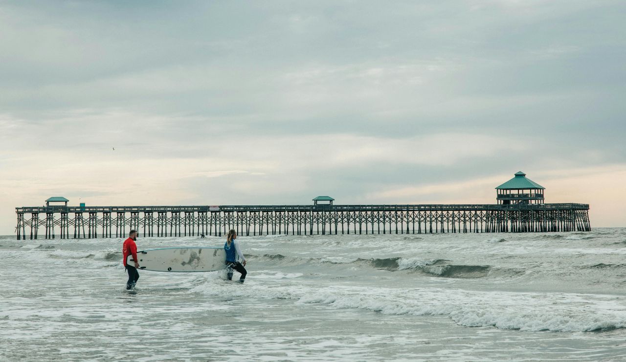 Surfboards on sandy Folly Beach with pier and ocean in background