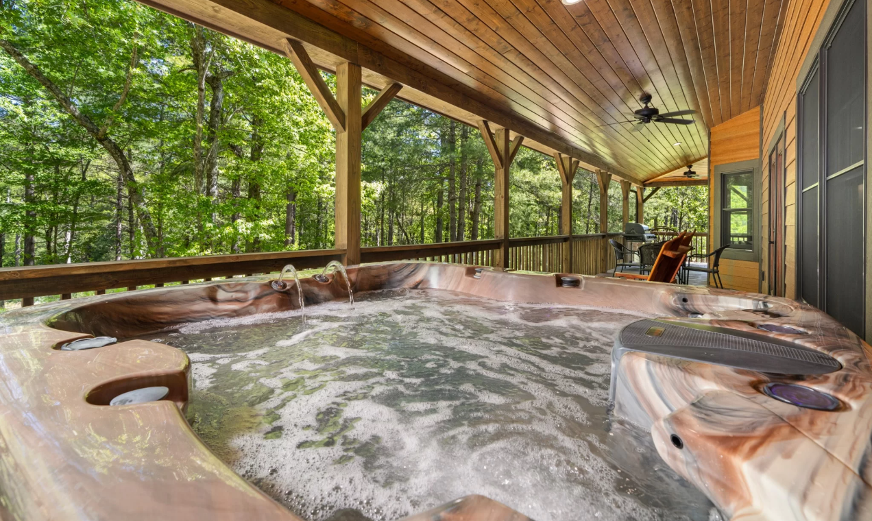 Bubbling jacuzzi on the back deck of a cabin surrounded by the woods.