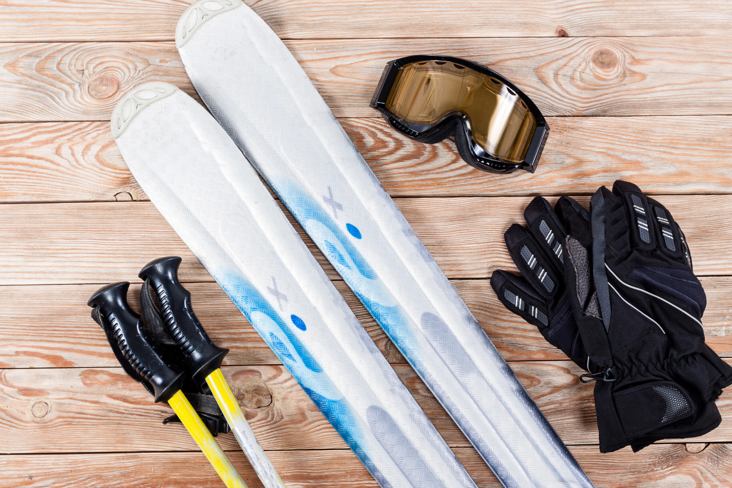 Two skis, ski poles, black gloves, and ski goggles rest on a wooden surface.