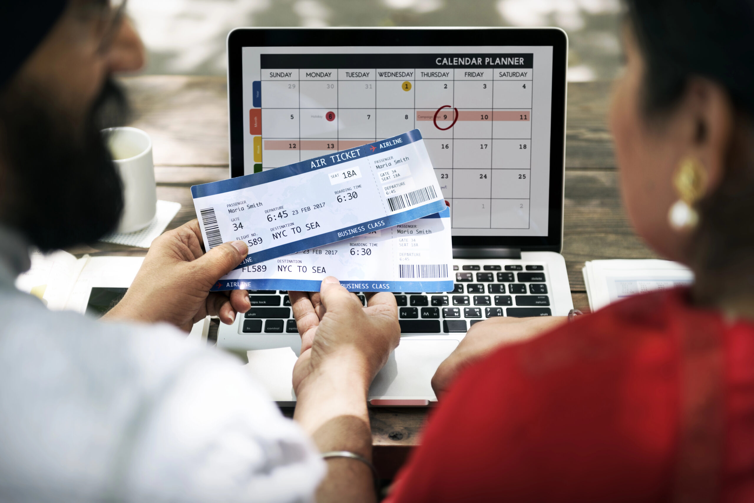 Two people holding airline tickets look at a laptop with a circled calendar date, planning the best days to book travel.