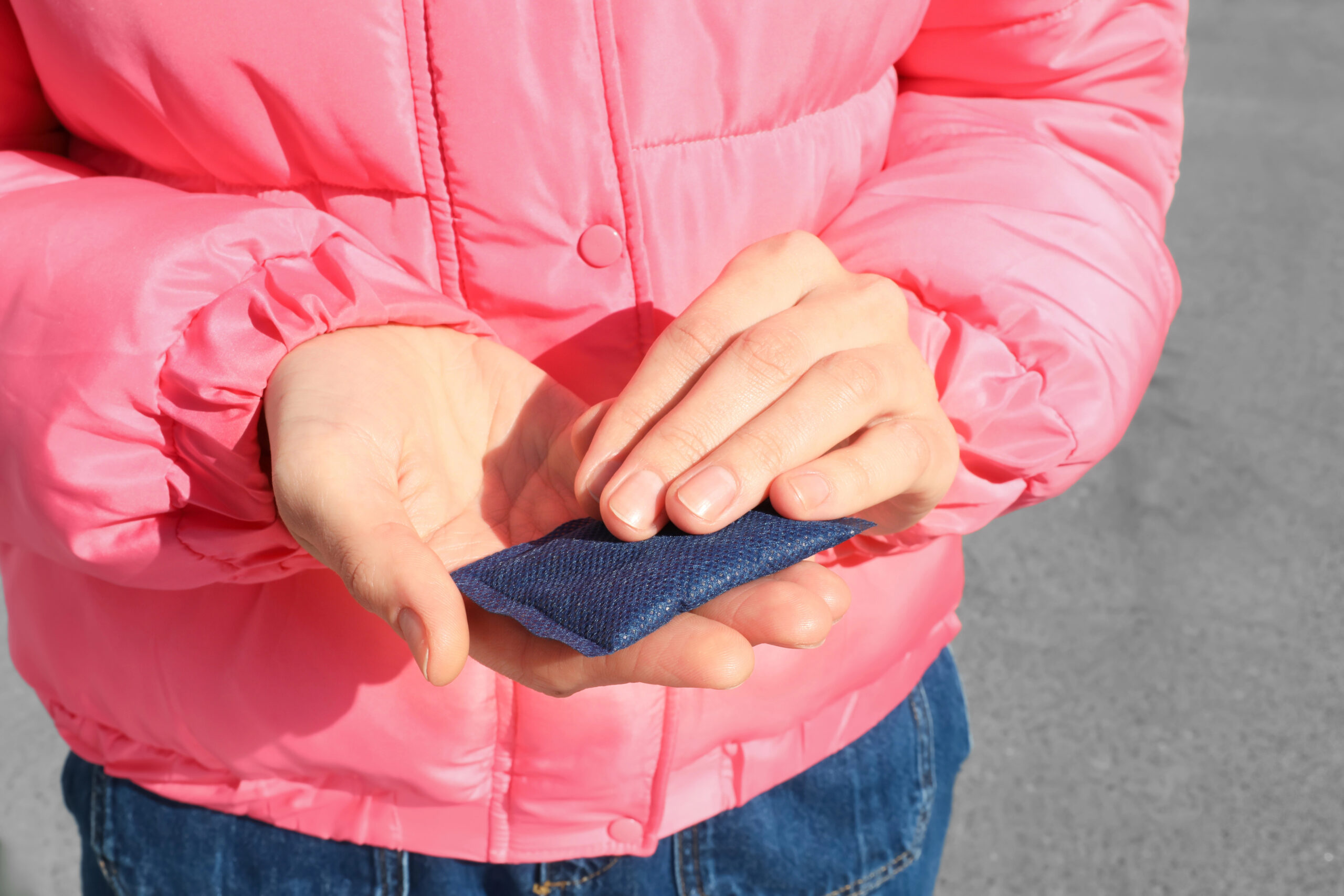 Outdoors, a person in a pink jacket holds a small denim fabric swatch.
