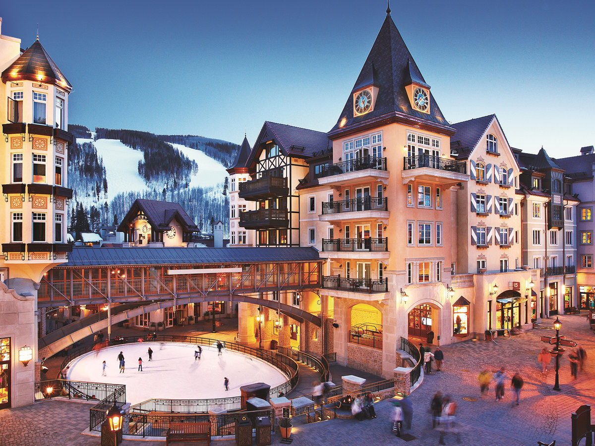People ice skate on an outdoor rink at dusk, bordered by The Arrabelle, one of the most romantic hotels in Vail.