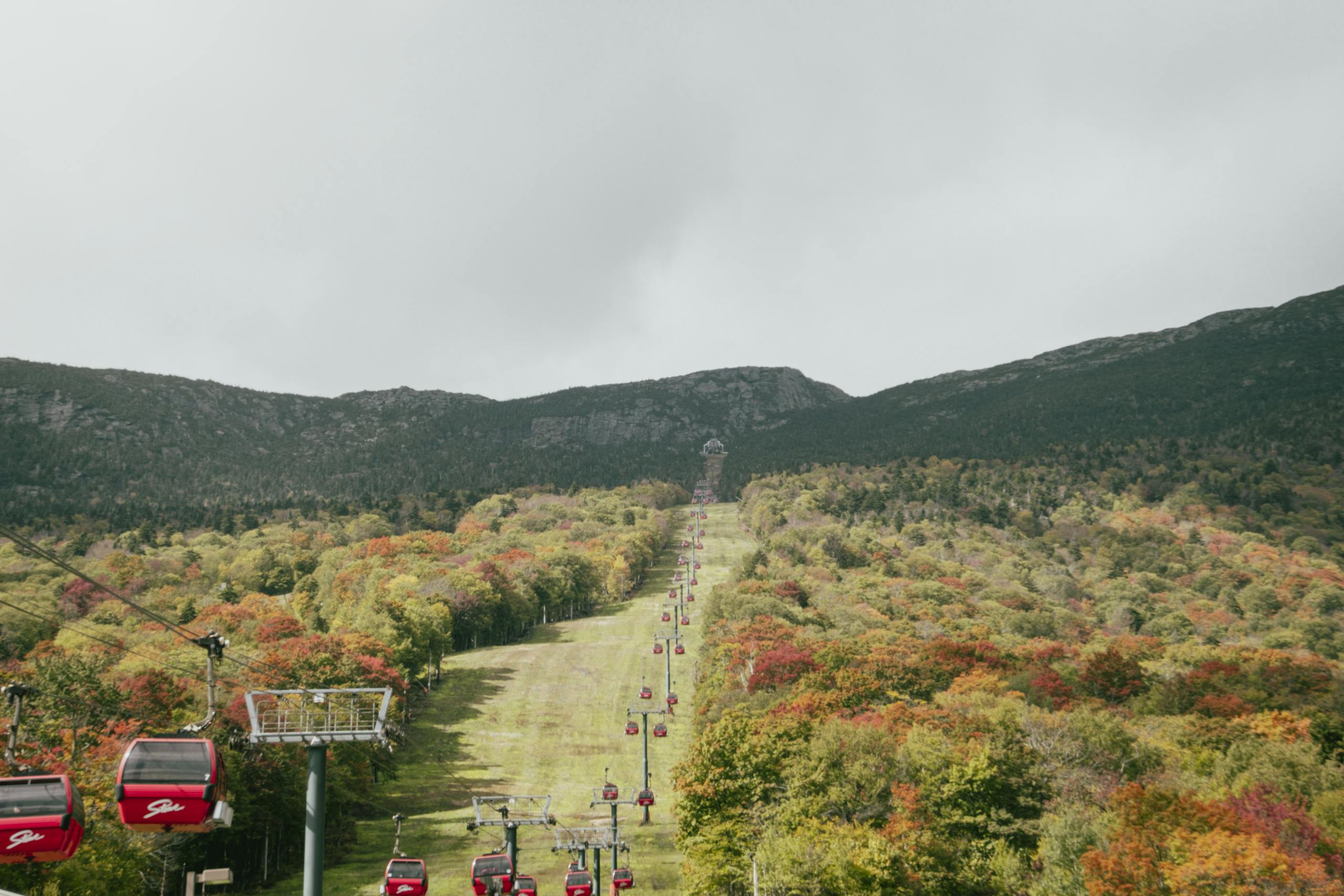 A stunning view of red gondolas ascending a forested mountain landscape in autumn.