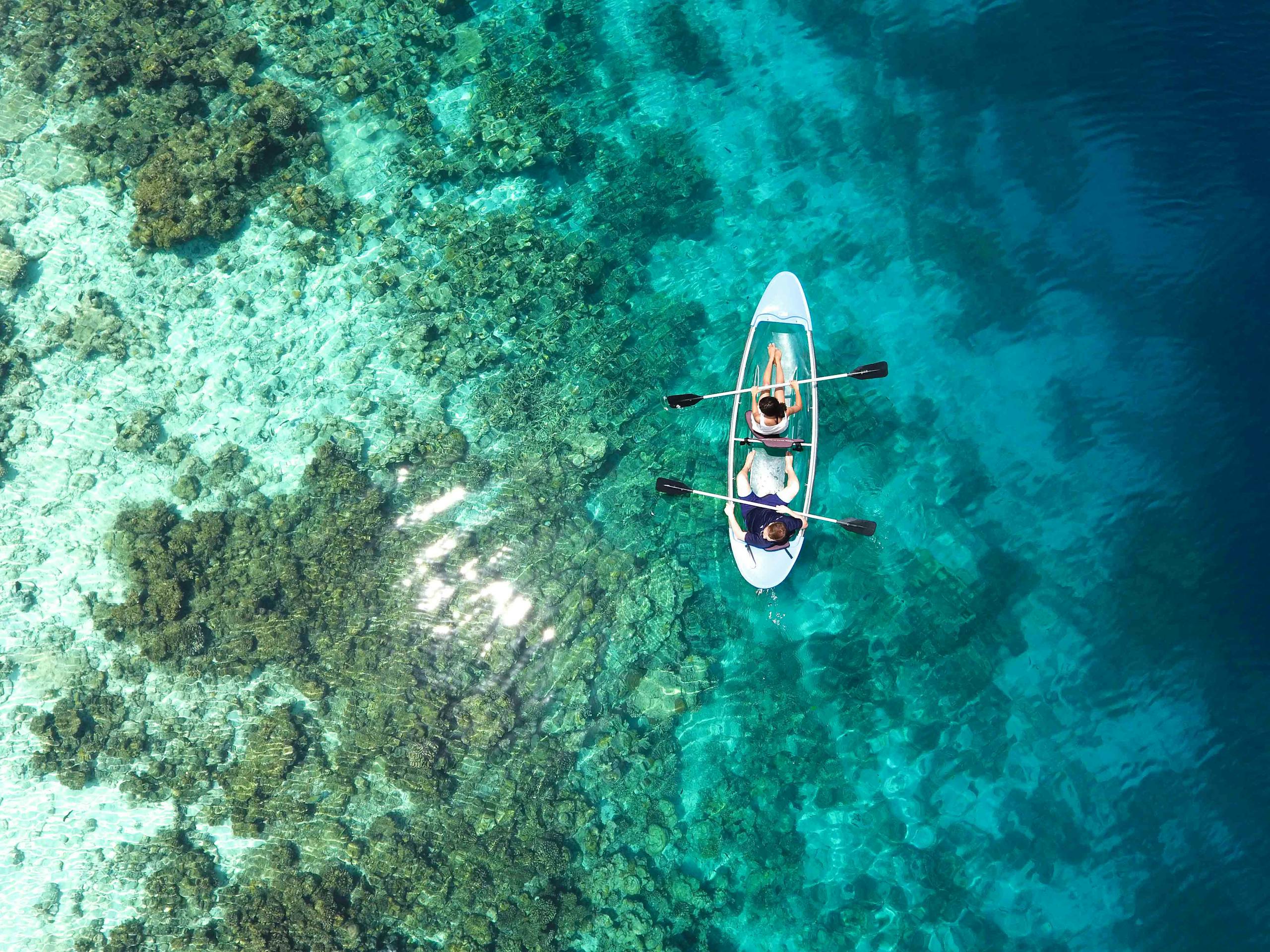 Aerial view of clear canoe gliding over vibrant coral reefs in the Maldives' turquoise waters.