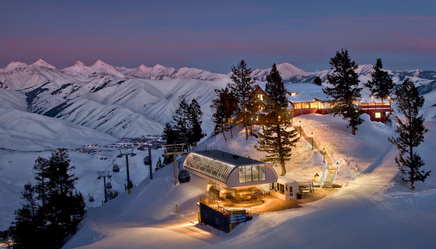 Sun Valley Resort at dusk with illuminated buildings, ski lift station, and distant mountains beneath a colorful sky. It's one of the most romantic ski resorts in the USA!