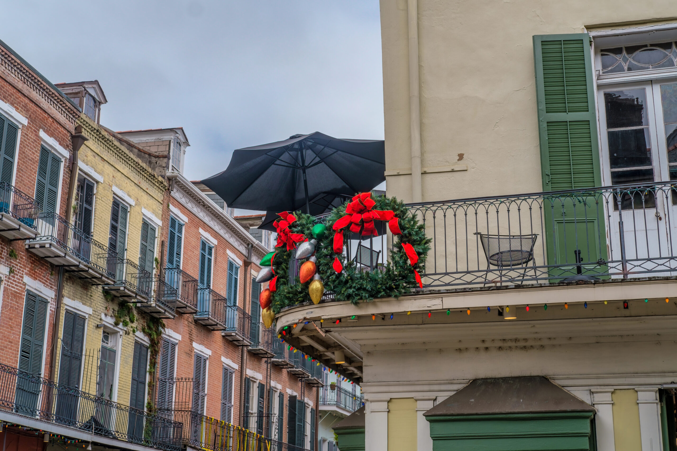 A balcony with green shutters is adorned with a wreath, red bows, ornaments, and an umbrella in New Orleans. It's one of the best Christmas vacations for couples!
