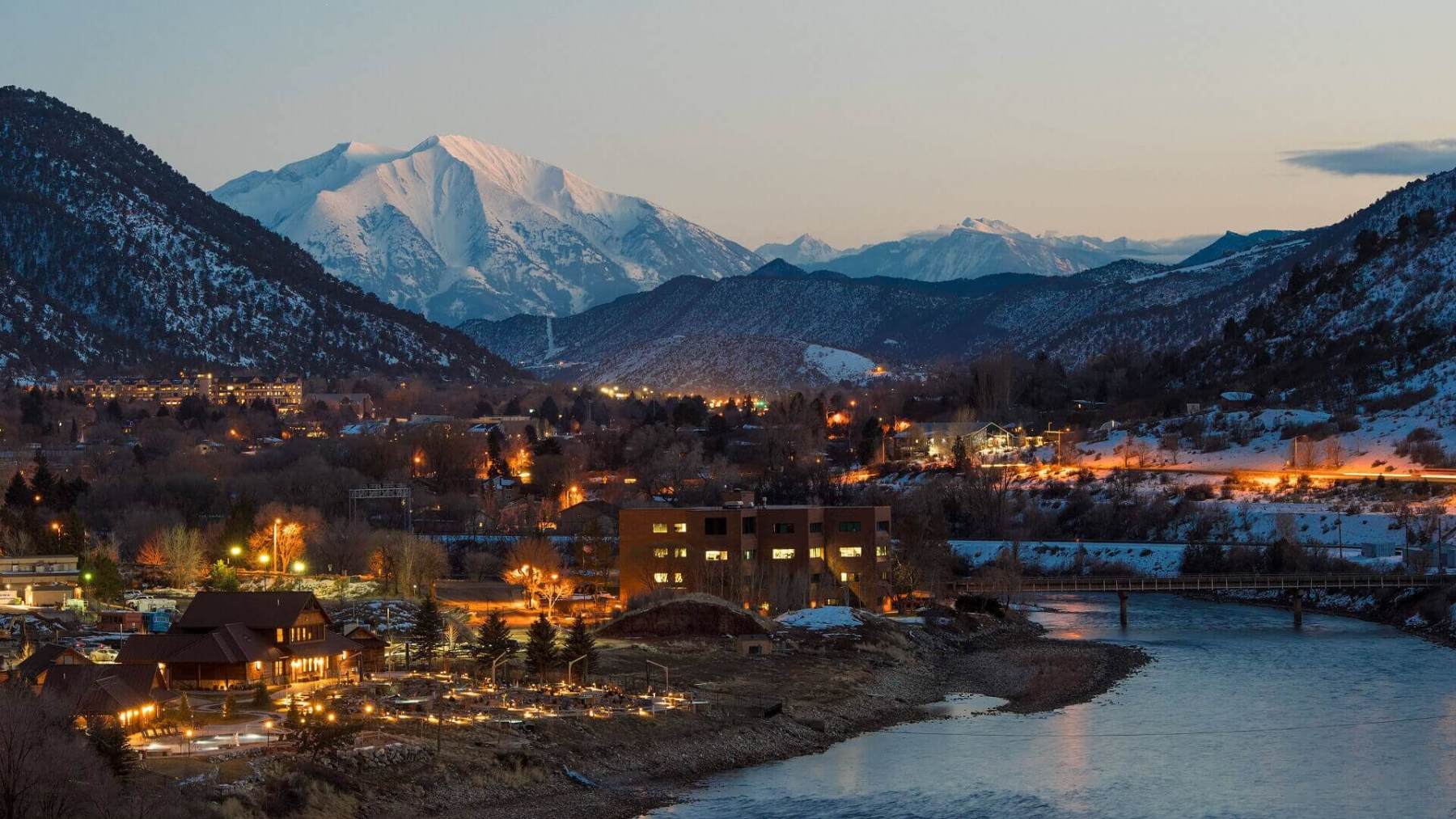 Snow-capped mountains tower over a lit-up Iron Mountain Hot Springs, one of the best things to do in Vail.