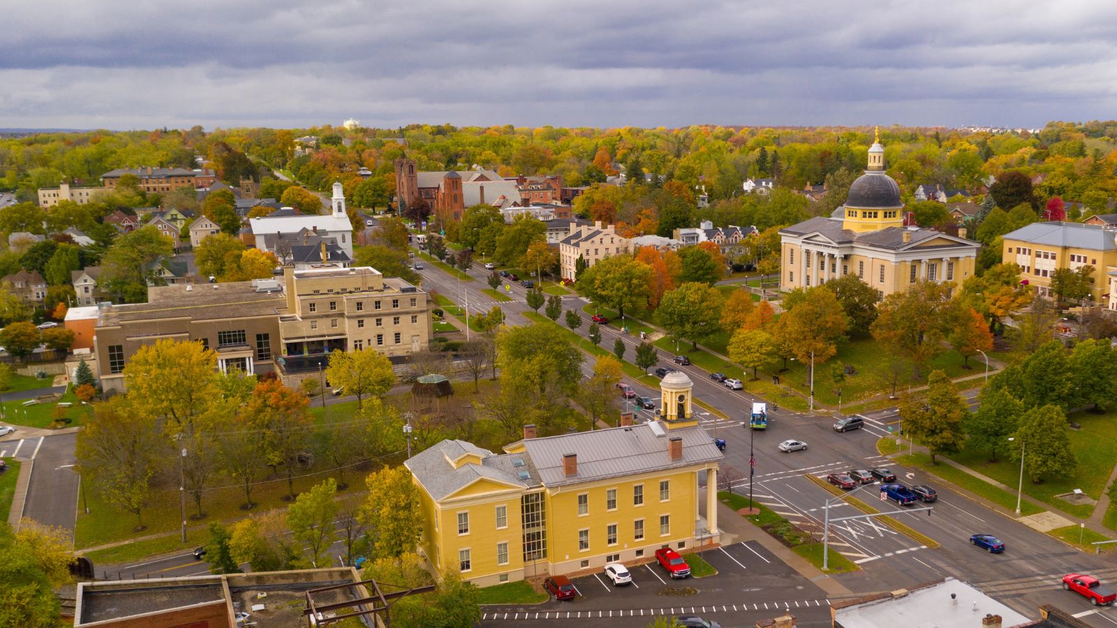 Aerial view of a small town with tree-lined streets, historic buildings, and a domed courthouse beneath cloudy autumn skies.