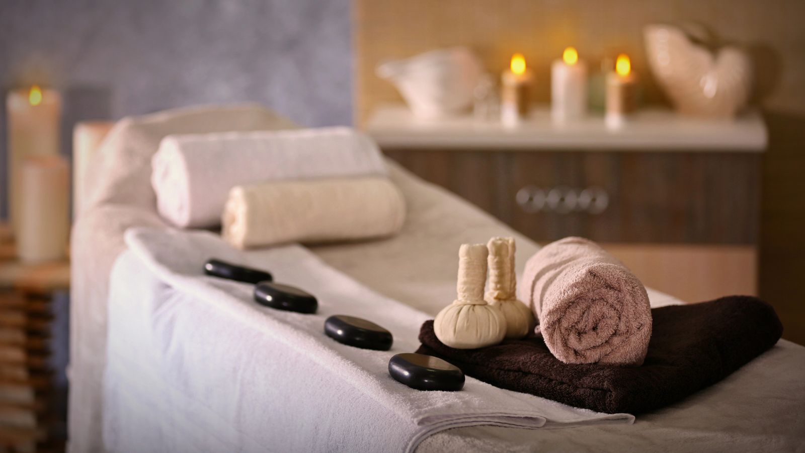A massage table with towels, hot stones, herbal compresses, and lit candles arranged for a spa-like atmosphere.