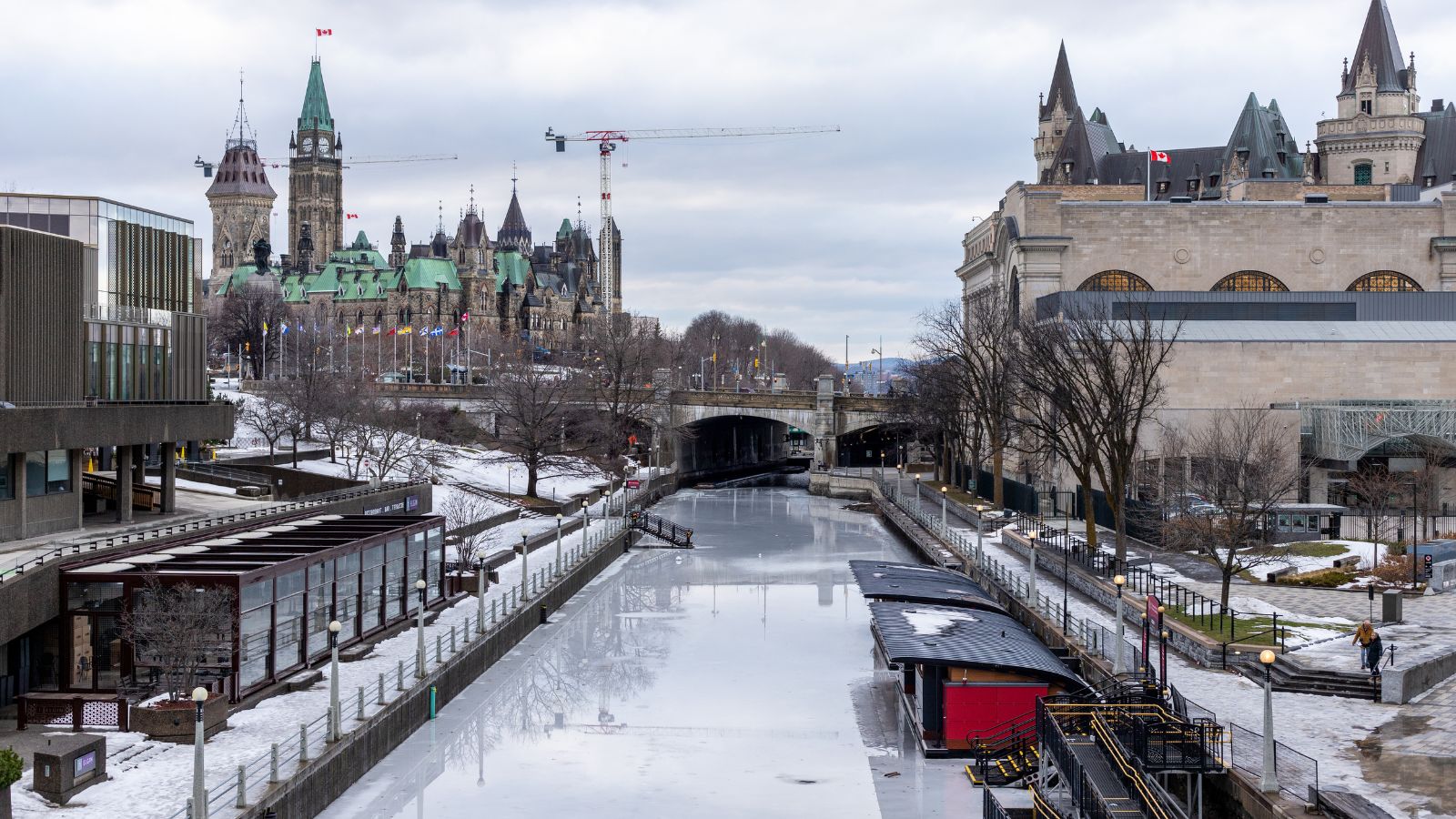 Ottawa’s partially frozen Rideau Canal in winter, with Parliament buildings beneath an overcast sky.