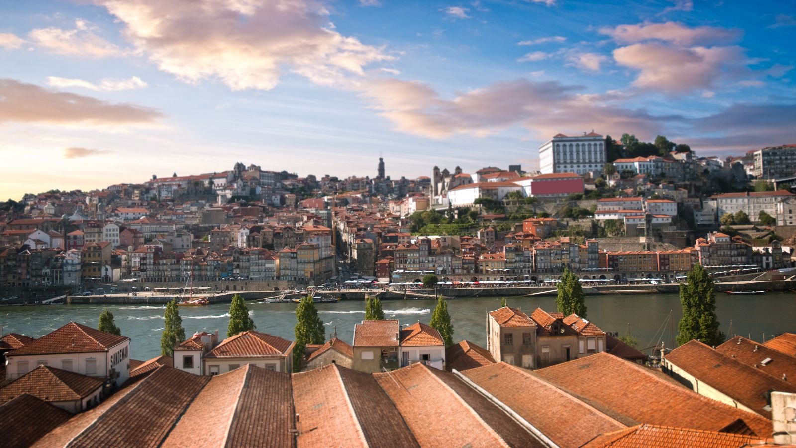 Porto cityscape with terracotta rooftops, the Douro River, and hillside historic buildings beneath a partly cloudy sky.