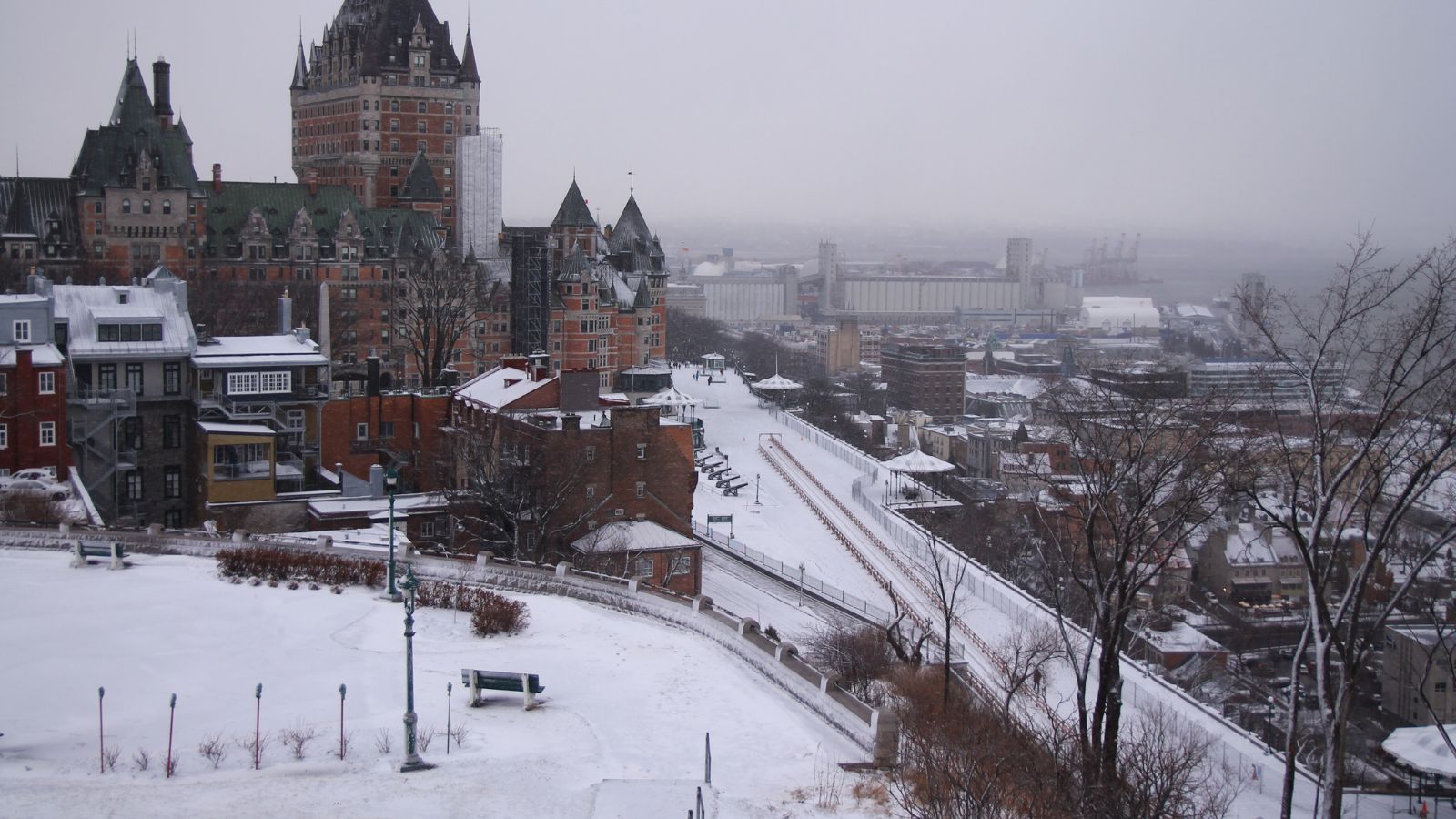 Quebec City’s snowy skyline features Château Frontenac, rooftops, bare trees, and a snow-covered path under cloudy skies.